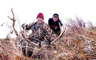 two men posing with elk and horns