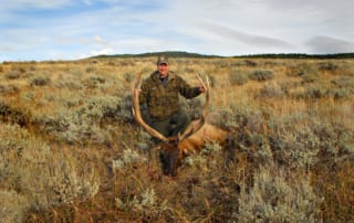 man posing with elk and horns in field