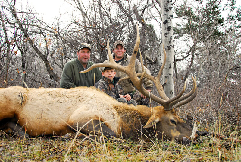 three men posing with elk and horns
