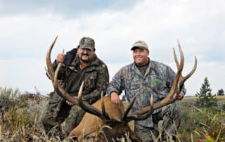 two men posing with elk and horns