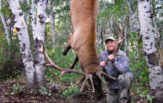 man posing with hangin elk and horns
