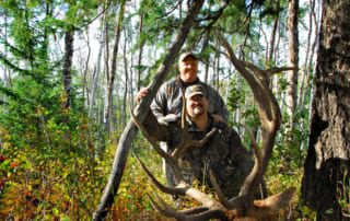two men posing with elk and horns