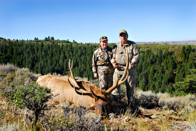 man & woman posing with elk and horns