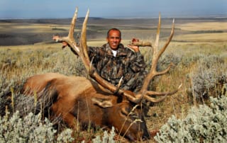 man in camo posing with elk and horns