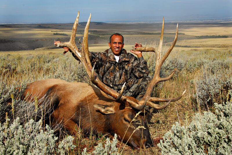 man in camo posing with elk and horns