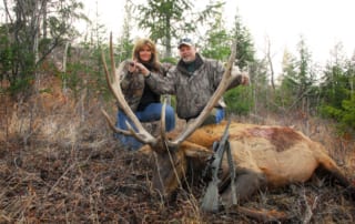 man and woman posing with elk and horns