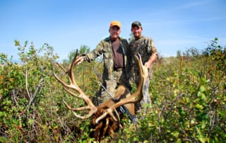 two men posing with elk and horns