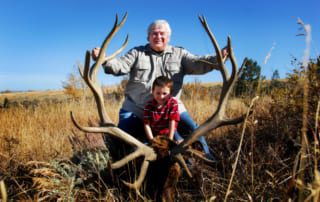 man and child posing with an elk and horns