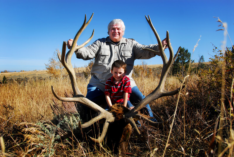 man and child posing with an elk and horns