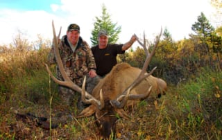 two men posing with an elk and horns
