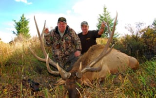 two men posing with an elk and horns