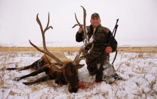 man posing with an elk and horns in winter snow