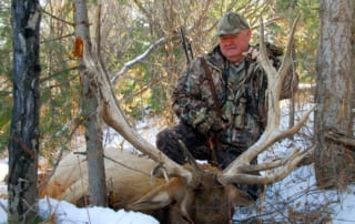man posing with an elk and horns in snow