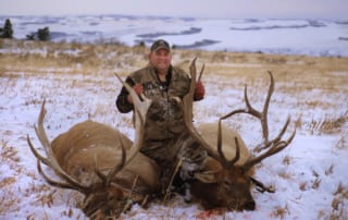man posing with an elk and horns in winter snow
