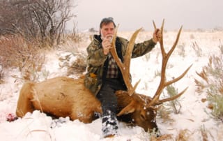 man posing with an elk and horns in winter