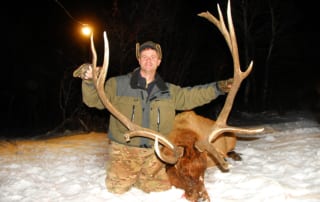 man posing with an elk and horns in snow