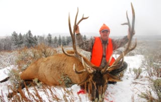 man posing with an elk and horns in winter