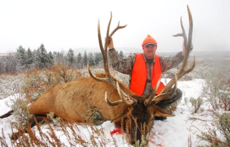 man posing with an elk and horns in winter