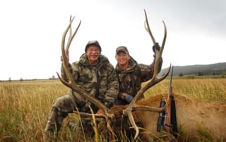 two men posing with an elk and horns