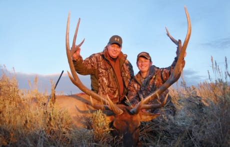 two men posing with an elk and horns