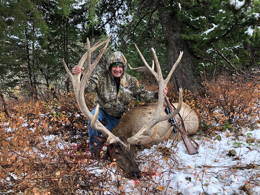 Man posing with large elk antlers.