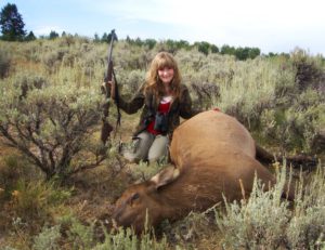 A girl posing with a dead elk after a successful hunting trip