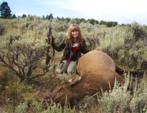 A girl posing with a dead elk after a successful hunting trip