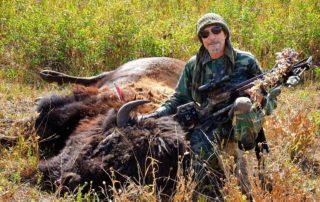A hunter posing with a buffalo after one of his buffalo hunts in Idaho