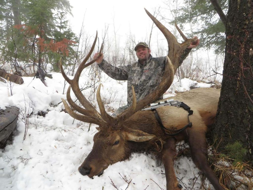 A man poses with a elk he shot hunting in snowy weather