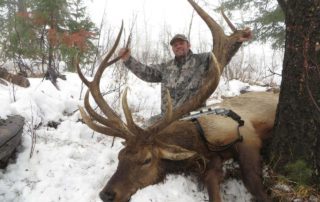 A man poses with a elk he shot hunting in snowy weather