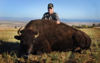 Buffalo Hunting: An avid hunter stands behind a large buffalo amid the Northern Idaho mountains at Rocky Mountain Elk Ranch.
