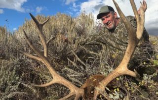 Elk Hunting Ranches: A seasoned elk hunter smiles while admiring the antlers of a massive bull elk in the Idaho mountains.