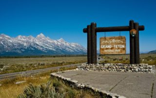 Grand Teton National Park: A sign standing at the entrance of an iconic national park with a large mountain in the background.