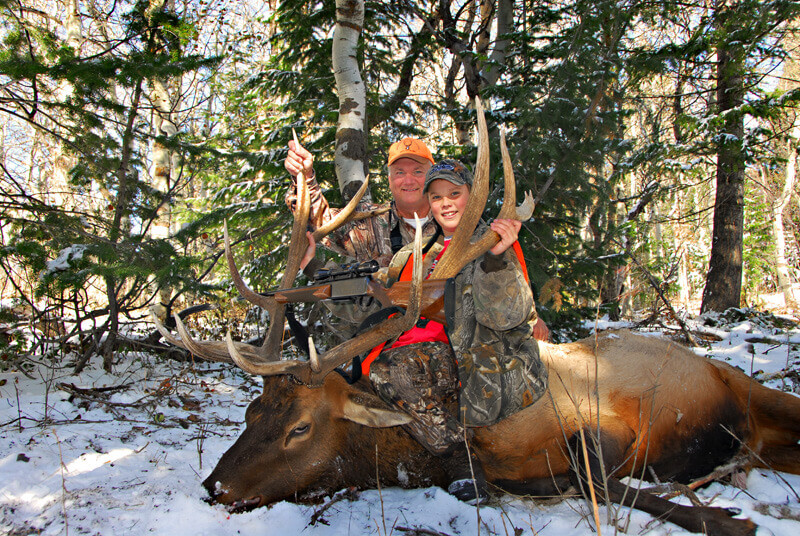A father and son pose with a massive elk during a winter hunting trip